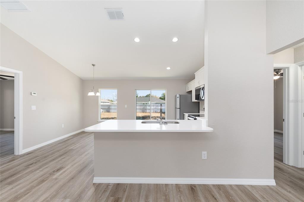 A kitchen with a white quartz breakfast bar, stainless steel appliances, and light wood flooring — 14260 SE 34TH COURT, SUMMERFIELD, FL