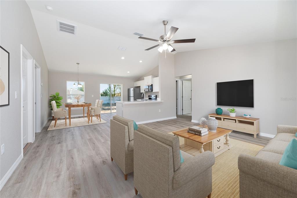 An open-concept living and dining area features light wood-look flooring and a vaulted ceiling — 14260 SE 34TH COURT, SUMMERFIELD, FL