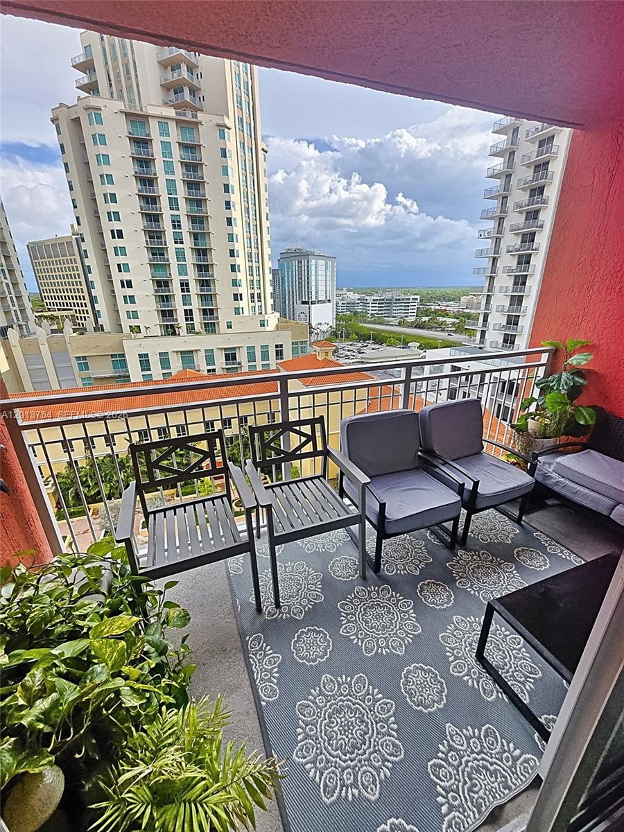A balcony with outdoor furniture, a patterned rug, potted plants, and a city skyline view — 7350 SW 89th St # 1506S, Miami FL 33156, MIAMI, FL