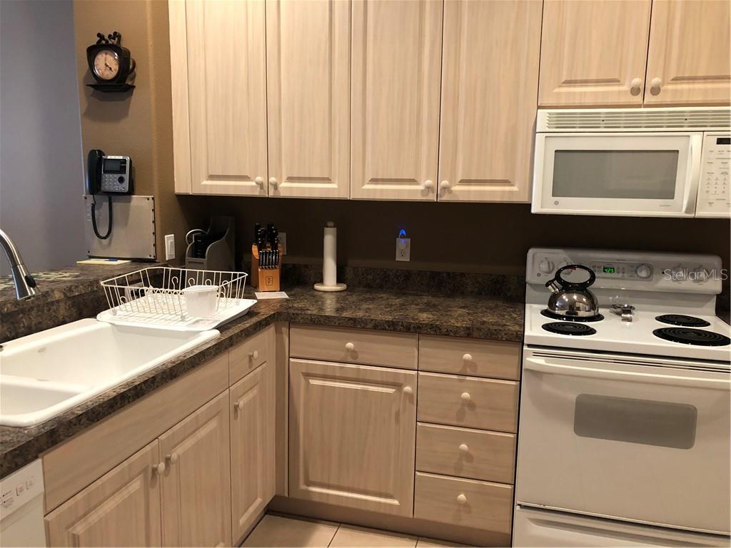 A kitchen features light wood cabinets, dark laminate countertops, and white appliances — 1838 SAN SILVESTRO DRIVE, VENICE, FL