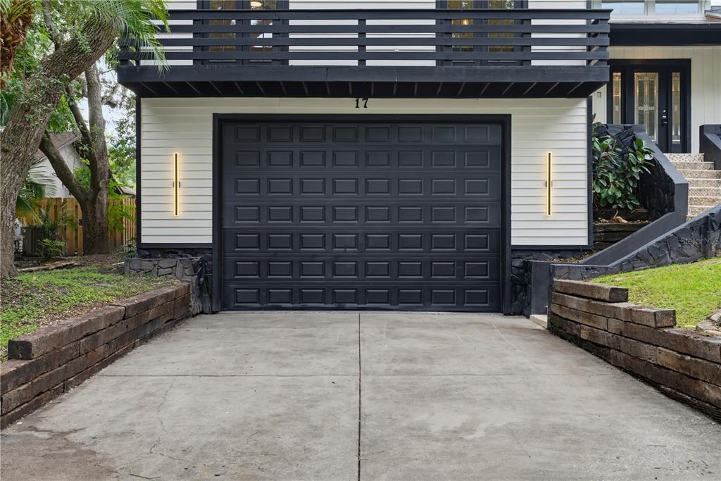 A black garage door sits below a balcony on a house with white horizontal siding — 17 PINEWOOD CIRCLE, SAFETY HARBOR, FL