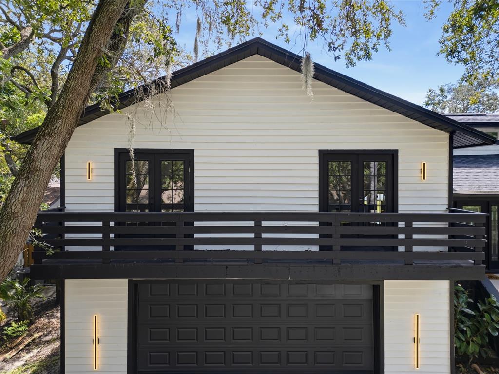 Exterior view of a two-story building with white siding, a black garage door, and a balcony — 17 PINEWOOD CIRCLE, SAFETY HARBOR, FL