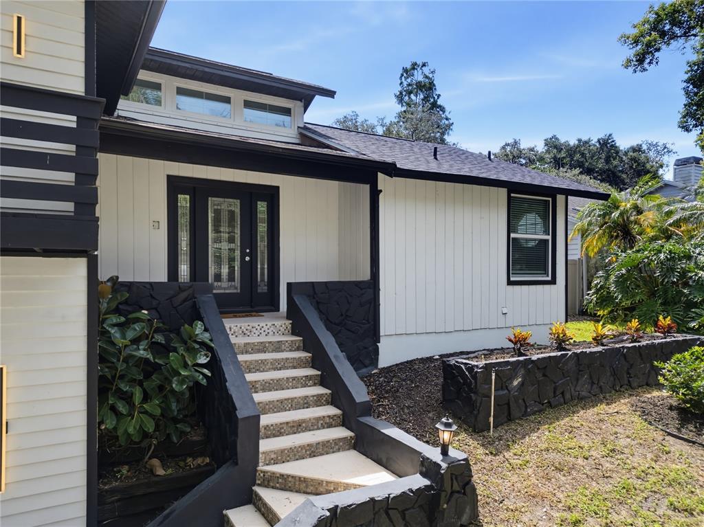 A white house exterior features a black-trimmed front door, stone accents, and concrete stairs — 17 PINEWOOD CIRCLE, SAFETY HARBOR, FL