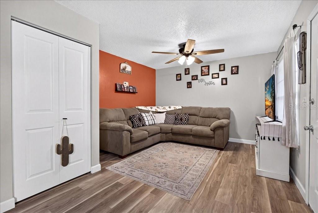 A living room features a brown sectional sofa, an orange accent wall, and wood-look flooring — 840 CENTER AVENUE UNIT 730, DAYTONA BEACH, FL