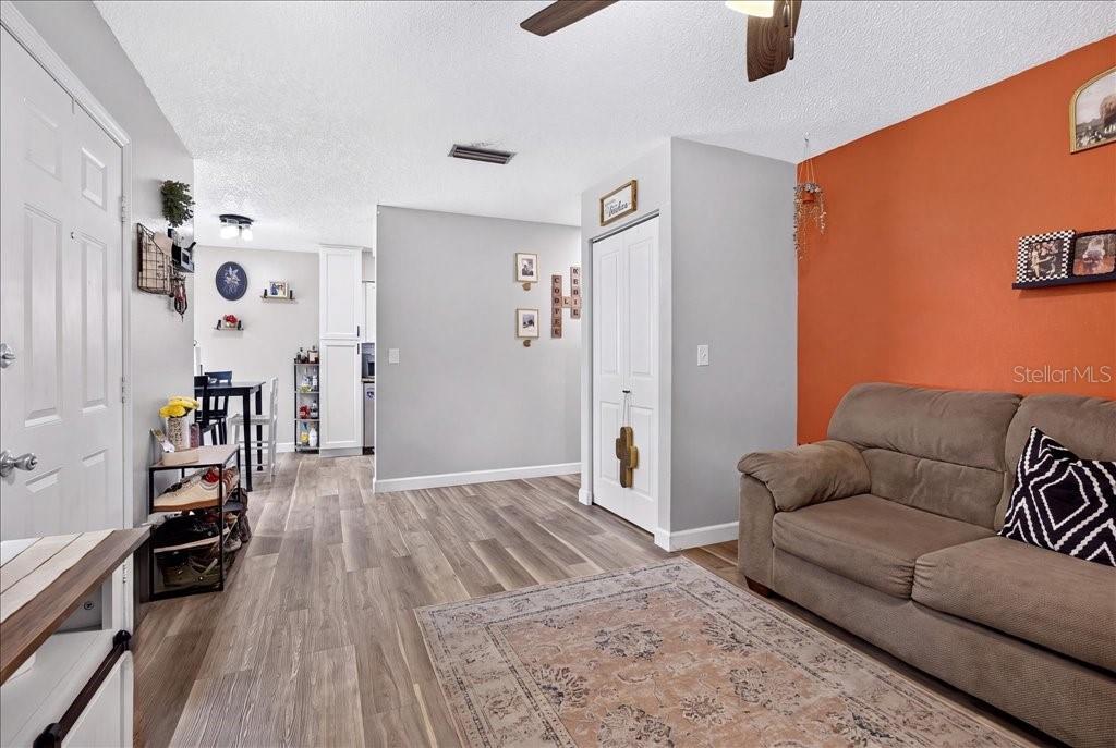 A living room with wood-look flooring, a brown sofa, and an orange accent wall — 840 CENTER AVENUE UNIT 730, DAYTONA BEACH, FL