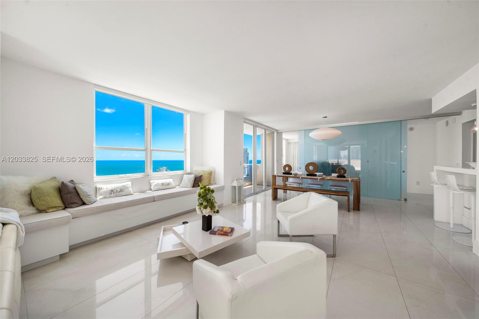 A bright living and dining area features white tile floors, ocean views, and modern furniture — 90 Alton Rd, Miami Beach FL 33139, MIAMI BEACH, FL
