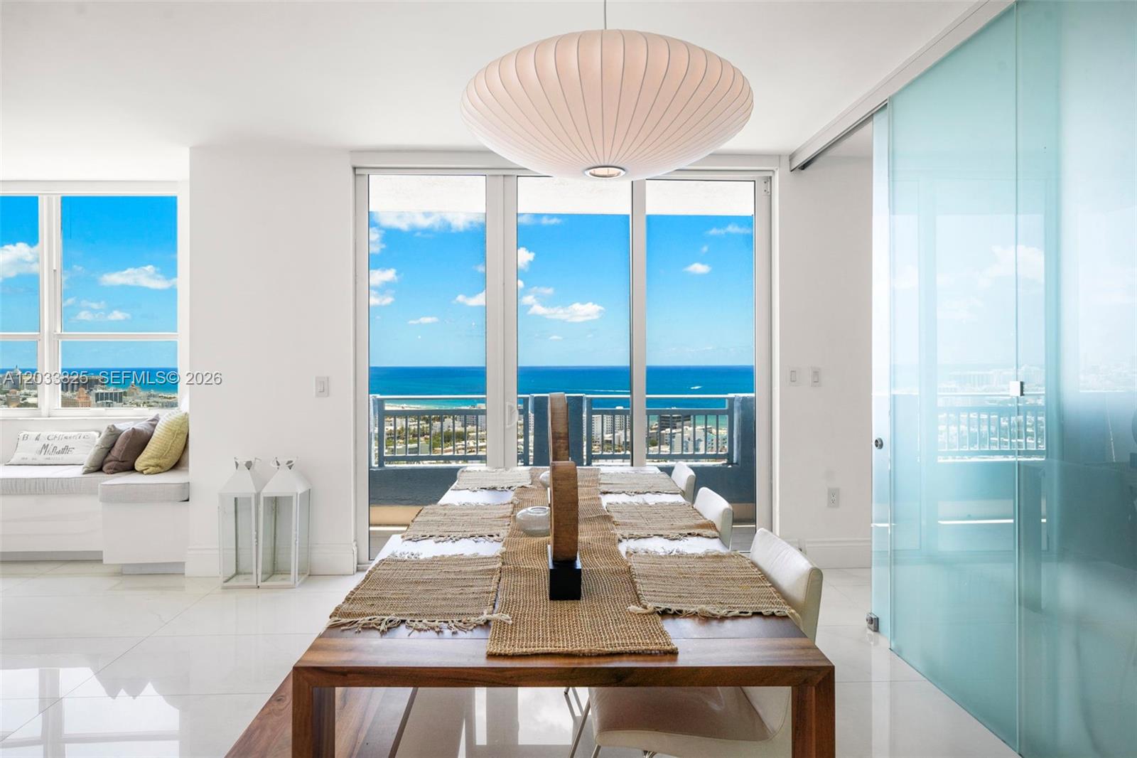 A dining room features a wooden table, a large pendant light, and floor-to-ceiling ocean views — 90 Alton Rd, Miami Beach FL 33139, MIAMI BEACH, FL