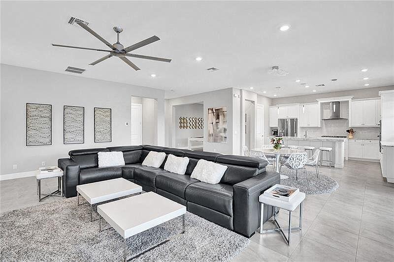 A modern open-concept living room features a large black sectional sofa and white kitchen cabinetry — 11720 Waterway Circle, Parkland FL 33076, PARKLAND, FL