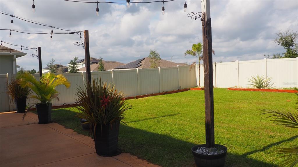 A backyard features a concrete patio, potted plants, string lights, and a white vinyl fence — 216 DENALI STREET, HAINES CITY, FL