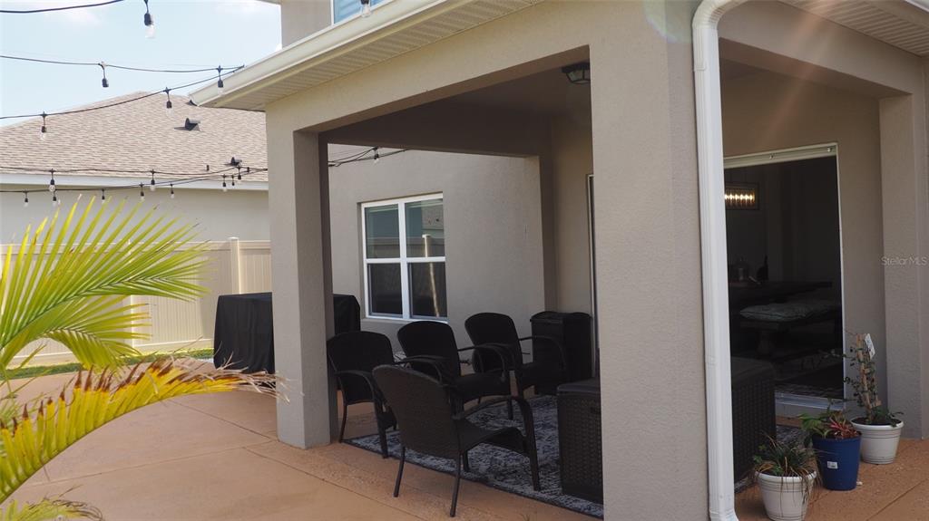 A covered patio features a concrete floor, outdoor seating, and string lights in a backyard — 216 DENALI STREET, HAINES CITY, FL