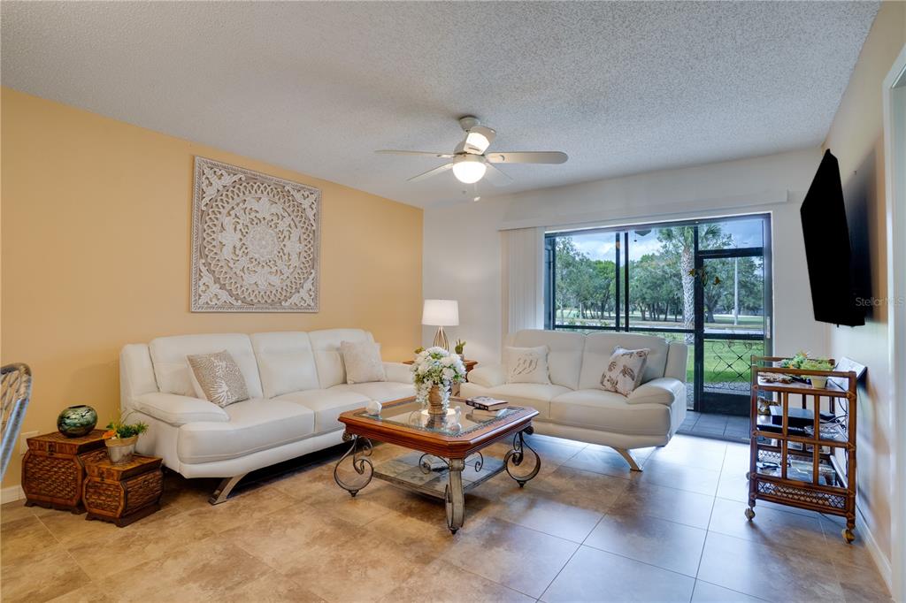 A living room features white leather sofas, a coffee table, and a sliding glass door — 117 E CYPRESS COURT UNIT 117, OLDSMAR, FL