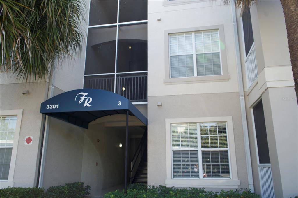 The exterior of a multi-story apartment building features a blue awning marked with 3301 — 3301 WHITESTONE CIRCLE UNIT 105, KISSIMMEE, FL