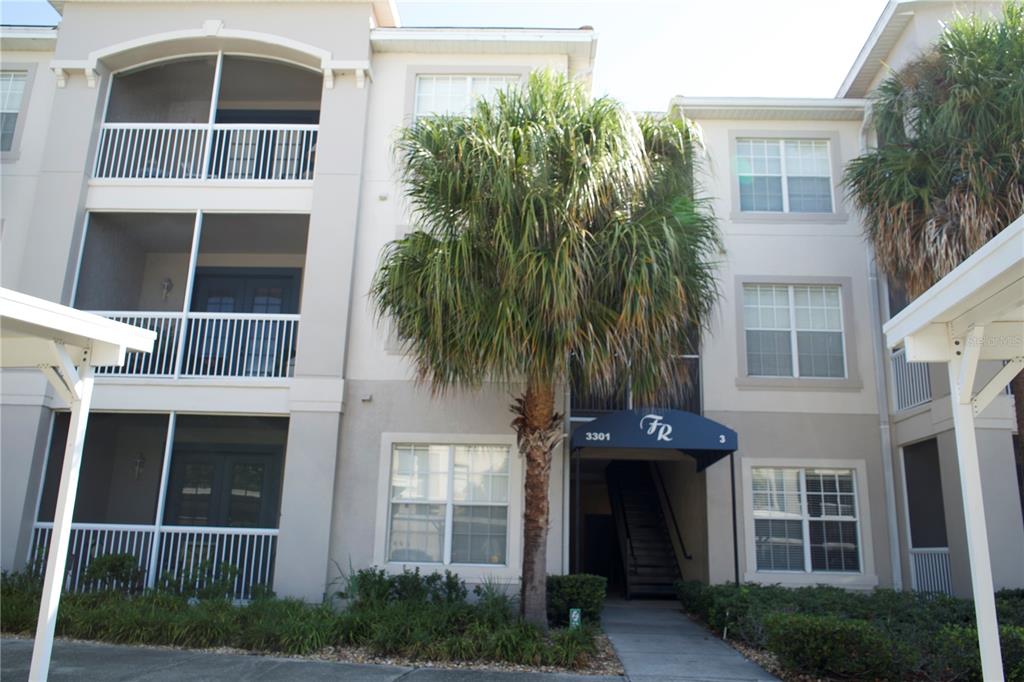 A three-story apartment building exterior features screened balconies, a palm tree, and a covered entrance — 3301 WHITESTONE CIRCLE UNIT 105, KISSIMMEE, FL