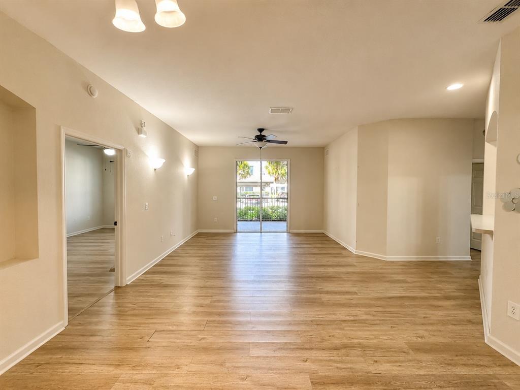A spacious living area features light wood-look flooring, a ceiling fan, and sliding glass doors — 3301 WHITESTONE CIRCLE UNIT 105, KISSIMMEE, FL
