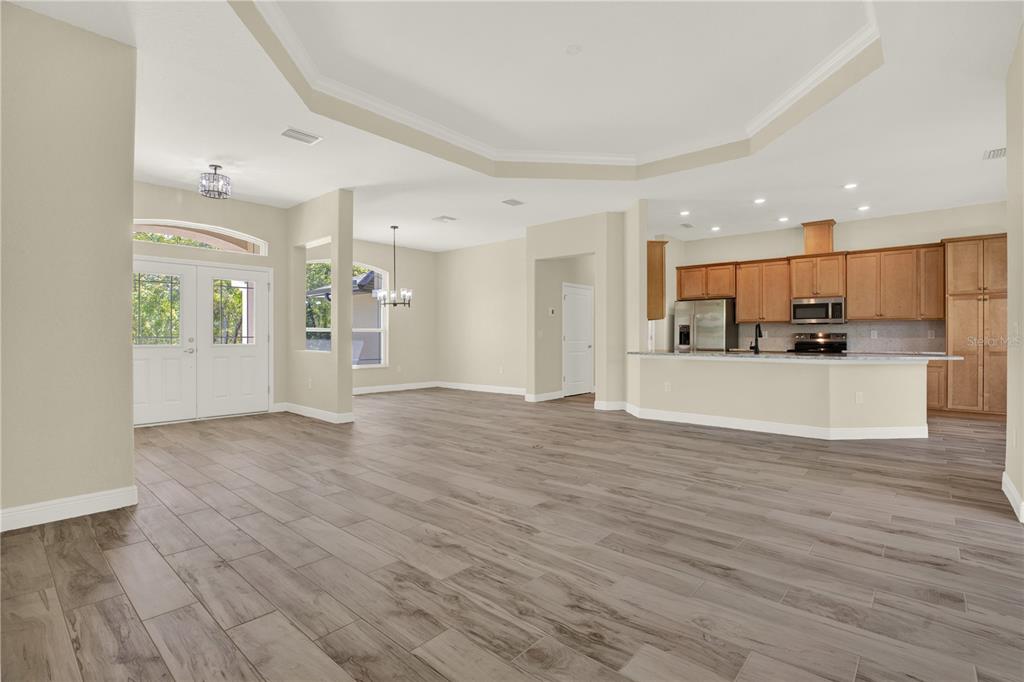 An open-concept living area features light wood-look tile flooring, a tray ceiling, and a kitchen — 12085 HARRIS HAWK ROAD, BROOKSVILLE, FL