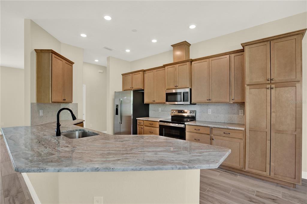 A kitchen features light wood cabinets, granite countertops, stainless steel appliances, and a breakfast bar — 12085 HARRIS HAWK ROAD, BROOKSVILLE, FL