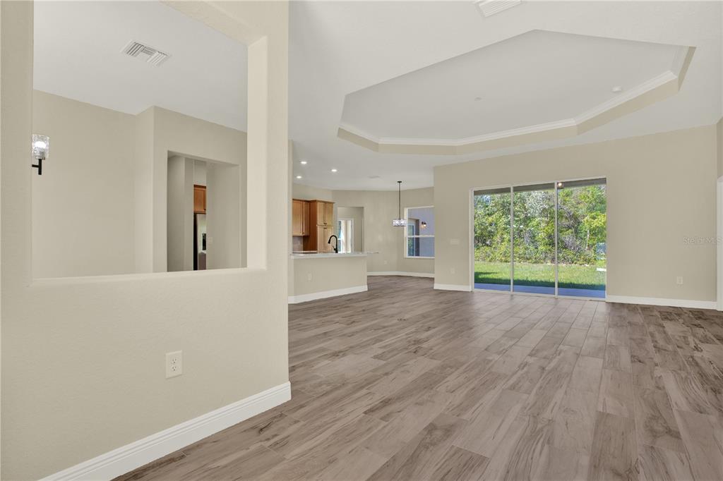 An open-concept living area features wood-look tile flooring, a tray ceiling, and sliding glass doors — 12085 HARRIS HAWK ROAD, BROOKSVILLE, FL