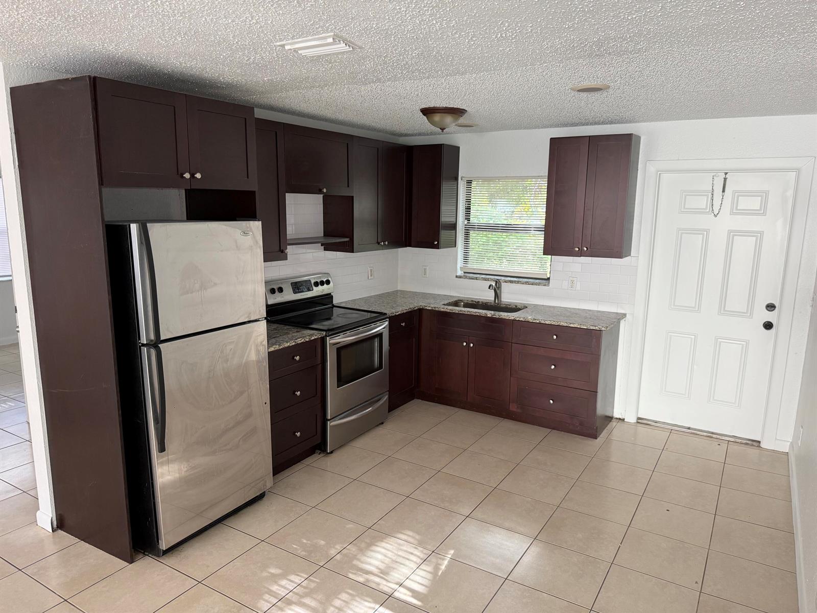 A kitchen features dark wood cabinets, stainless steel appliances, granite countertops, and light tile flooring — 336 NE 12th Avenue, Boynton Beach FL 33435, BOYNTON BEACH, FL