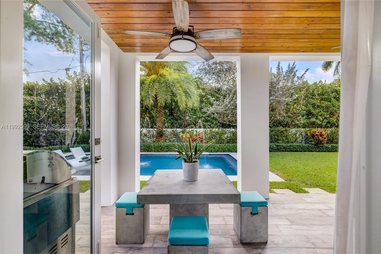 A covered patio features a concrete table with blue-cushioned stools, a ceiling fan, and pool — 5602 SW 65th Ct, South Miami FL 33143, SOUTH MIAMI, FL