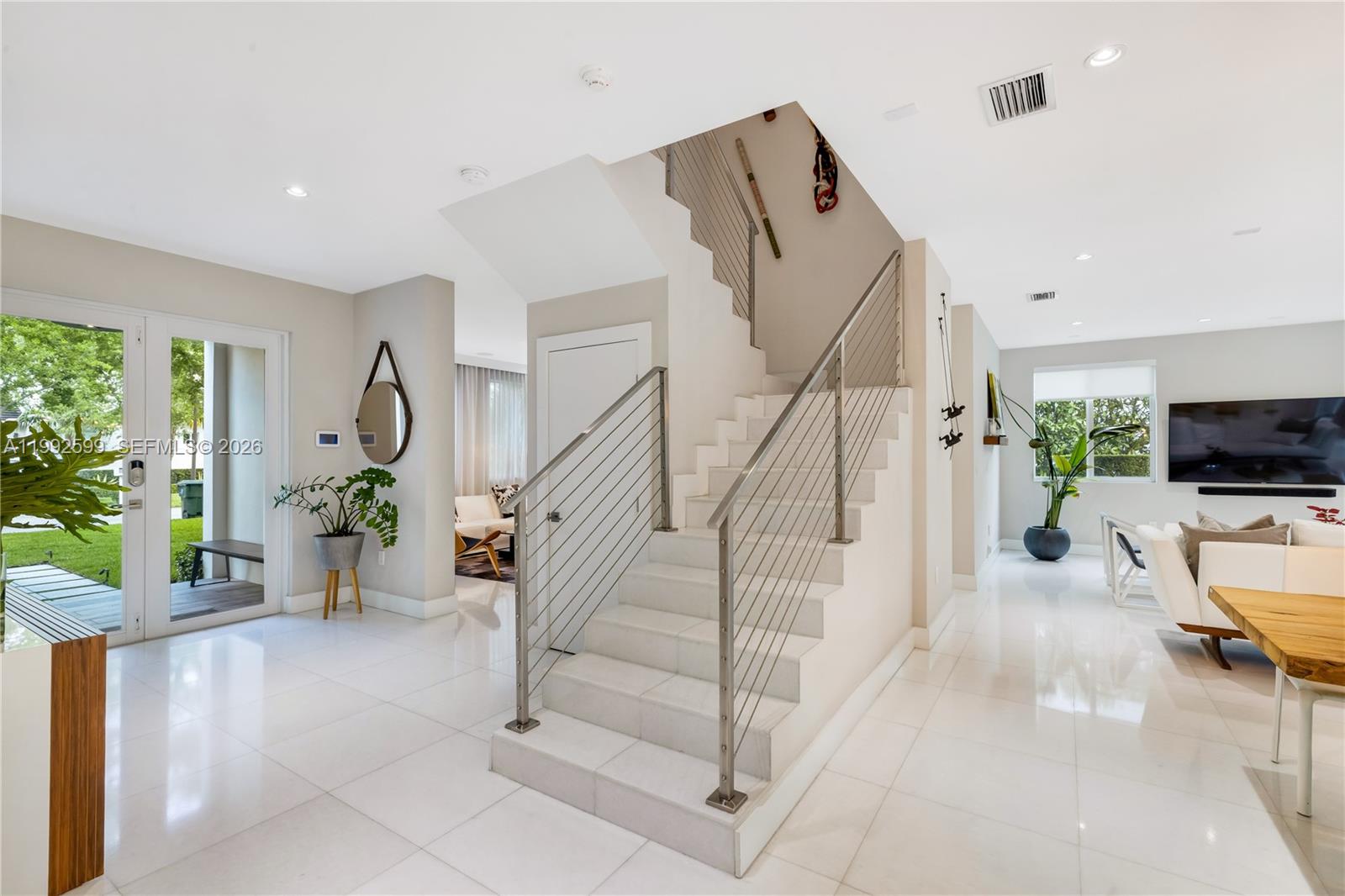 A bright, modern entryway features white tile floors, a central staircase, and glass doors — 5602 SW 65th Ct, South Miami FL 33143, SOUTH MIAMI, FL