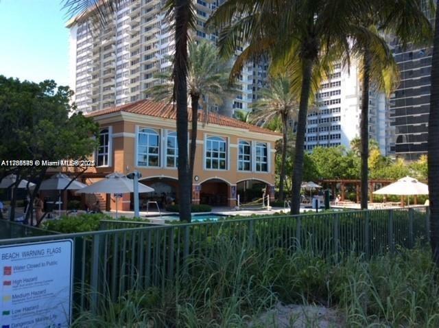 A tan building with arched openings sits behind a fence near tall palm trees — 2080 S Ocean Dr # 707, Hallandale Beach FL 33009, HALLANDALE BEACH, FL