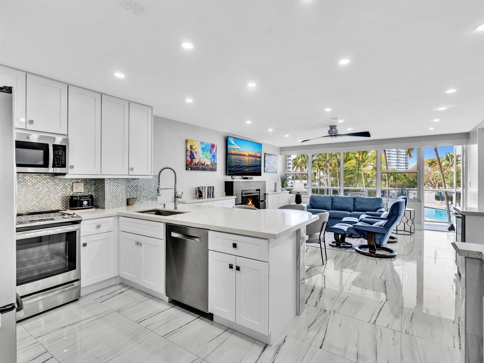 A modern white kitchen with stainless steel appliances opens into a living room with pool views — 3300 NE 36th Street # 217, FL 33308, FL