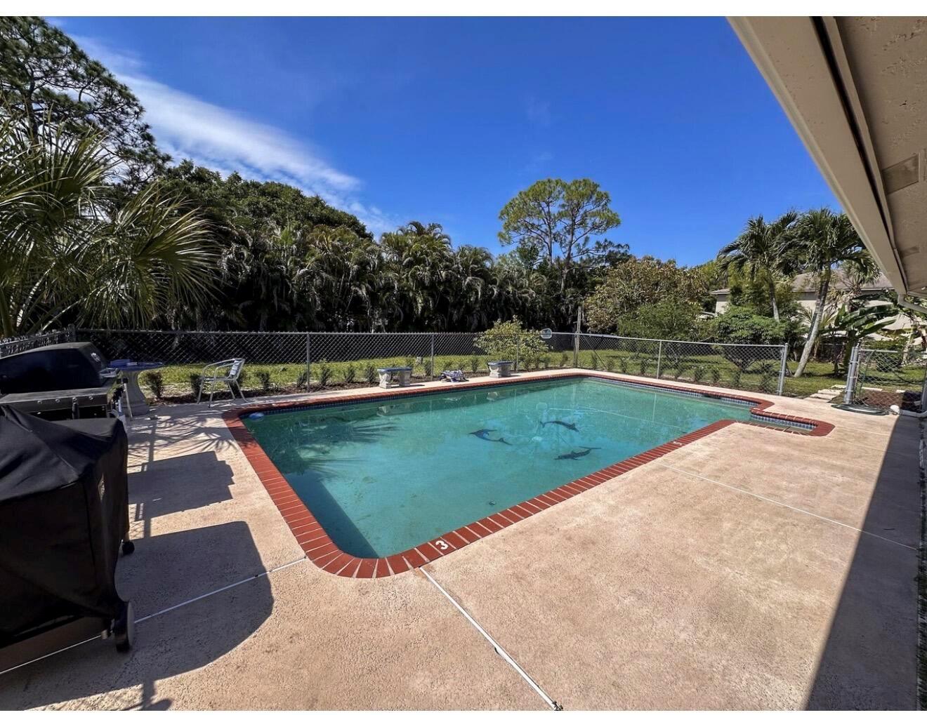 A rectangular swimming pool with a red brick border sits in a fenced backyard — 8264 Palomino Drive, Lake Worth FL 33467, LAKE WORTH, FL