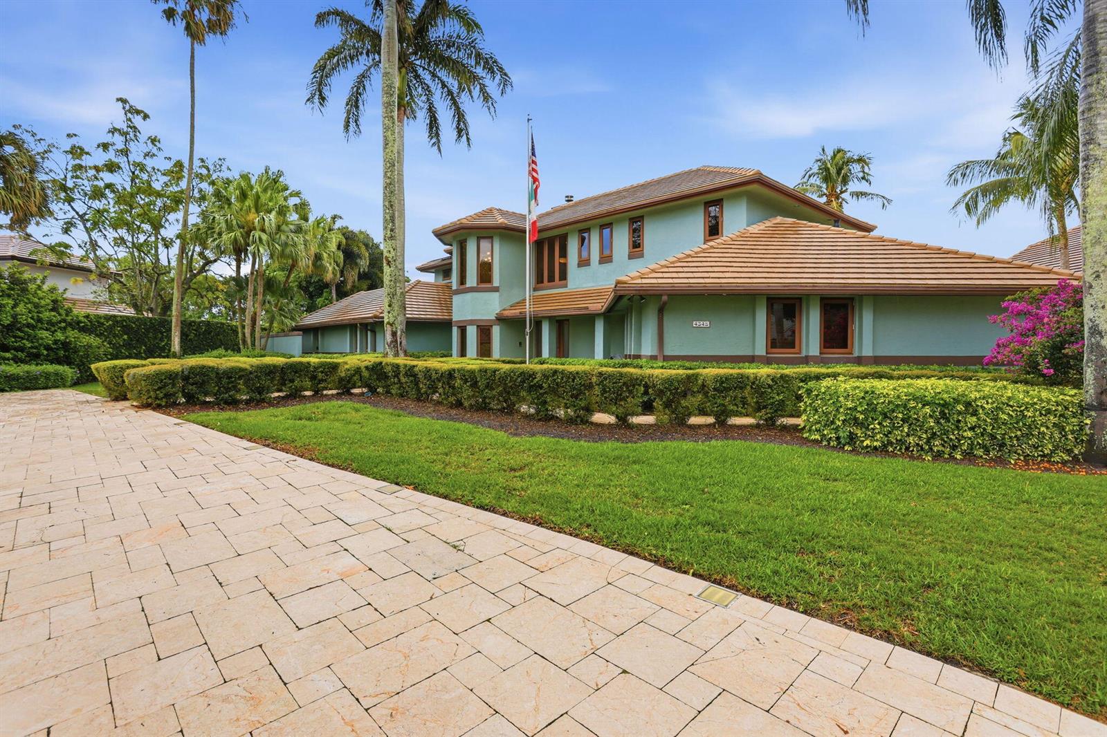 A two-story house with a tiled roof and green exterior stands behind a manicured hedge — 4348 Saint Andrews Drive, Boynton Beach FL 33436, BOYNTON BEACH, FL