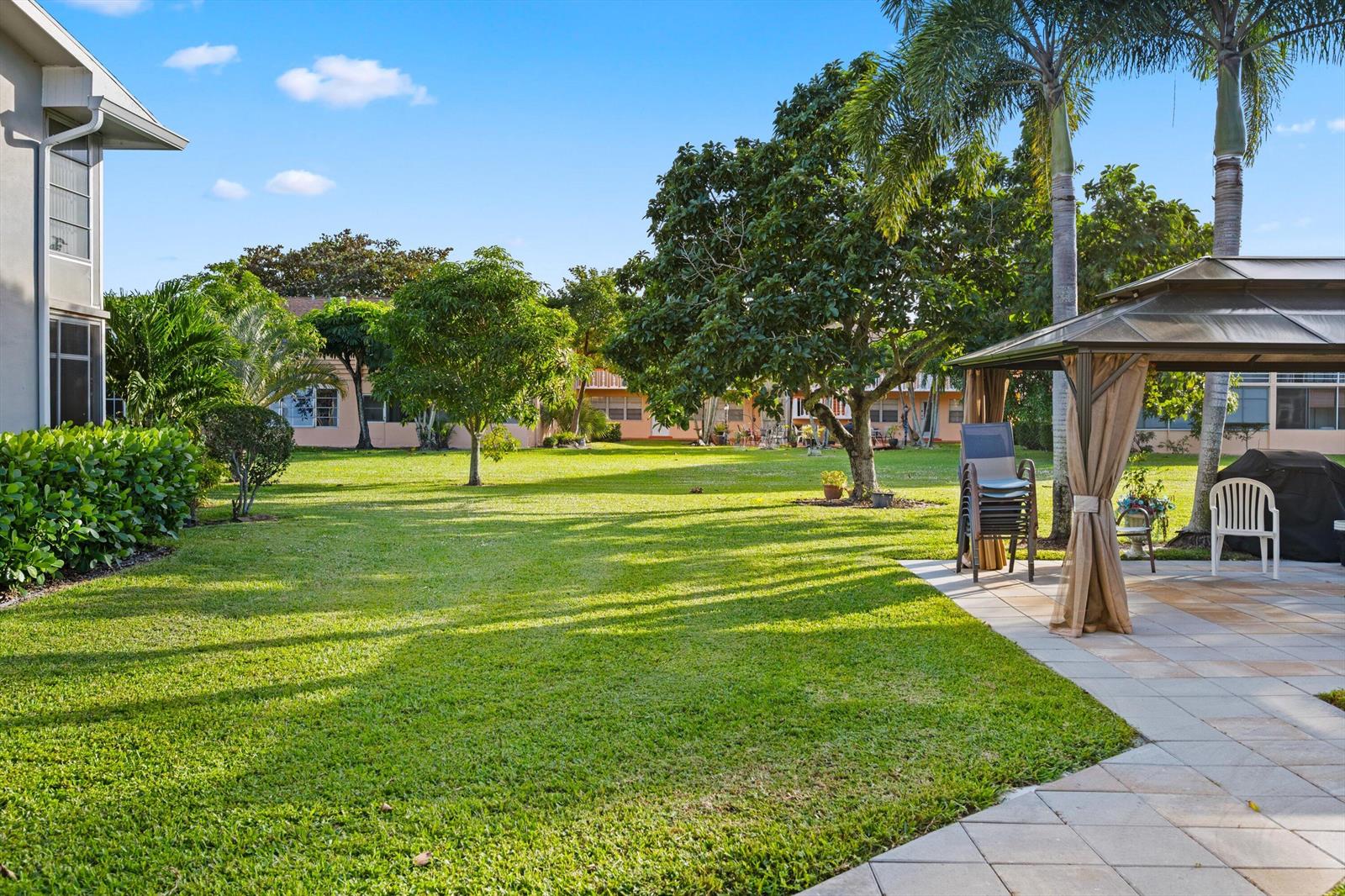 A grassy backyard features a paved patio, a gazebo, and several trees under a blue sky — 380 Sheffield P, West Palm Beach FL 33417, WEST PALM BEACH, FL