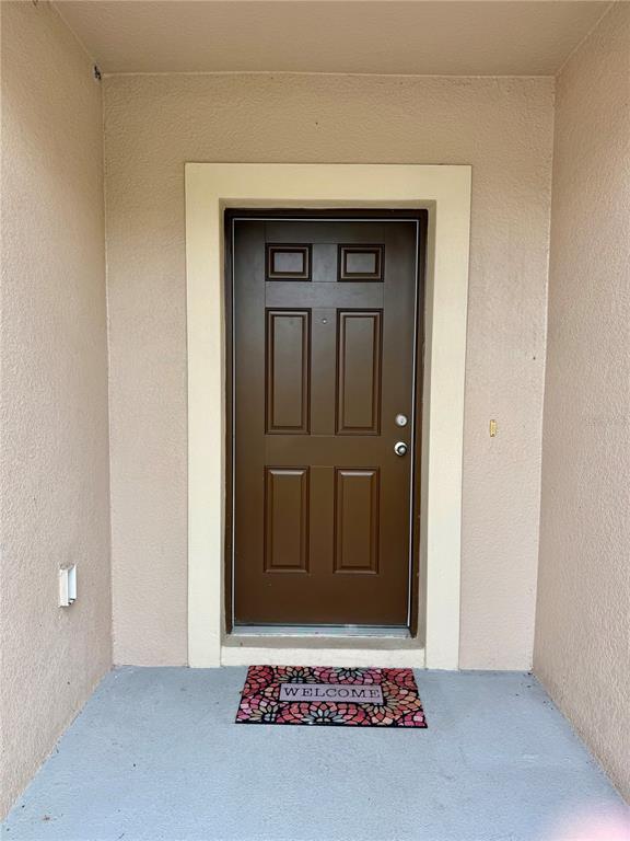 A brown six-panel front door is centered within a beige entryway with a welcome mat — 196 TRACY COURT E, HAINES CITY, FL
