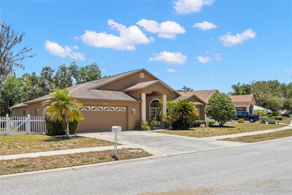 A tan, single-story suburban house with a two-car garage and a white picket fence — 4638 ANACONDA DRIVE, NEW PORT RICHEY, FL