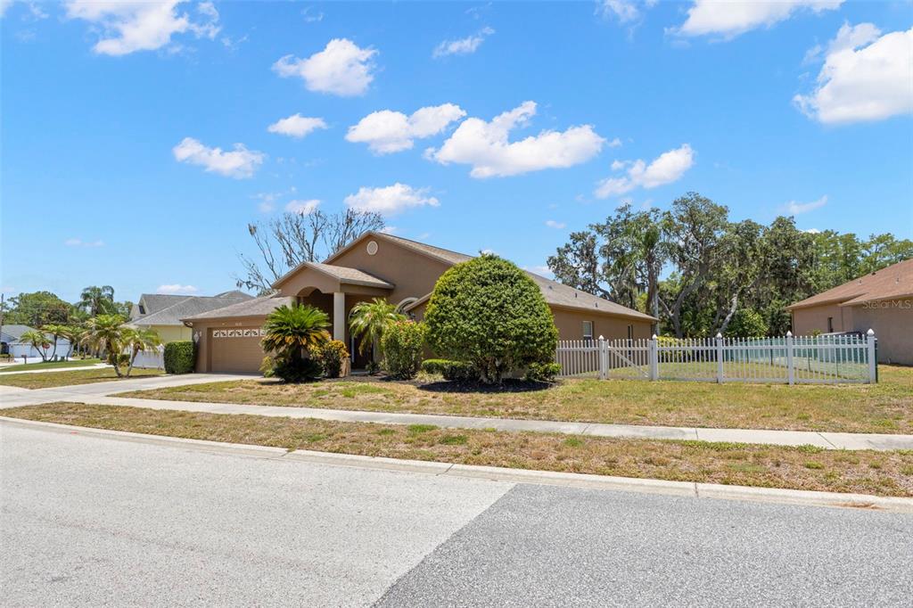 A tan single-story house with a white fence and a large bush in the yard — 4638 ANACONDA DRIVE, NEW PORT RICHEY, FL