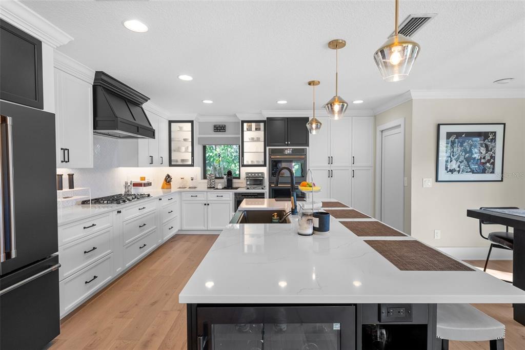 A modern kitchen features white cabinets, black accents, stainless steel appliances, and light wood flooring — 4926 W MELROSE AVENUE N, TAMPA, FL
