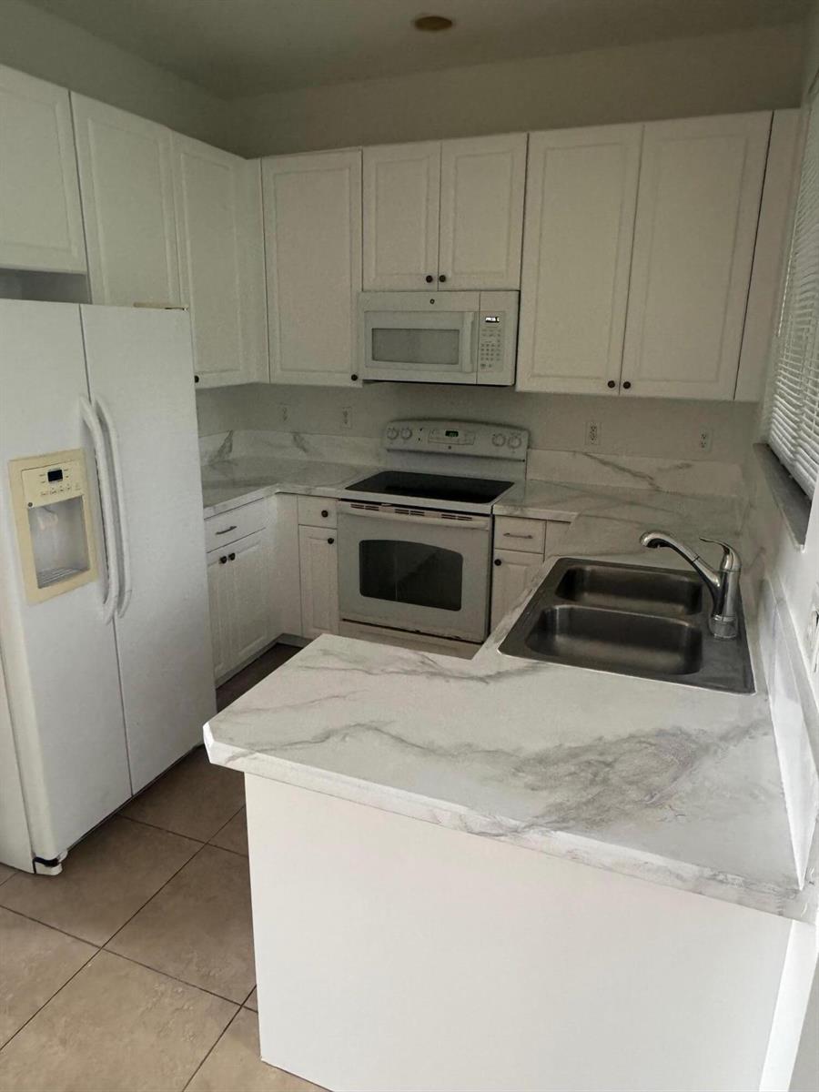 A kitchen features white cabinets, marble-look countertops, and white appliances — 4459 Cotswold Hills Drive, FL 33461, FL
