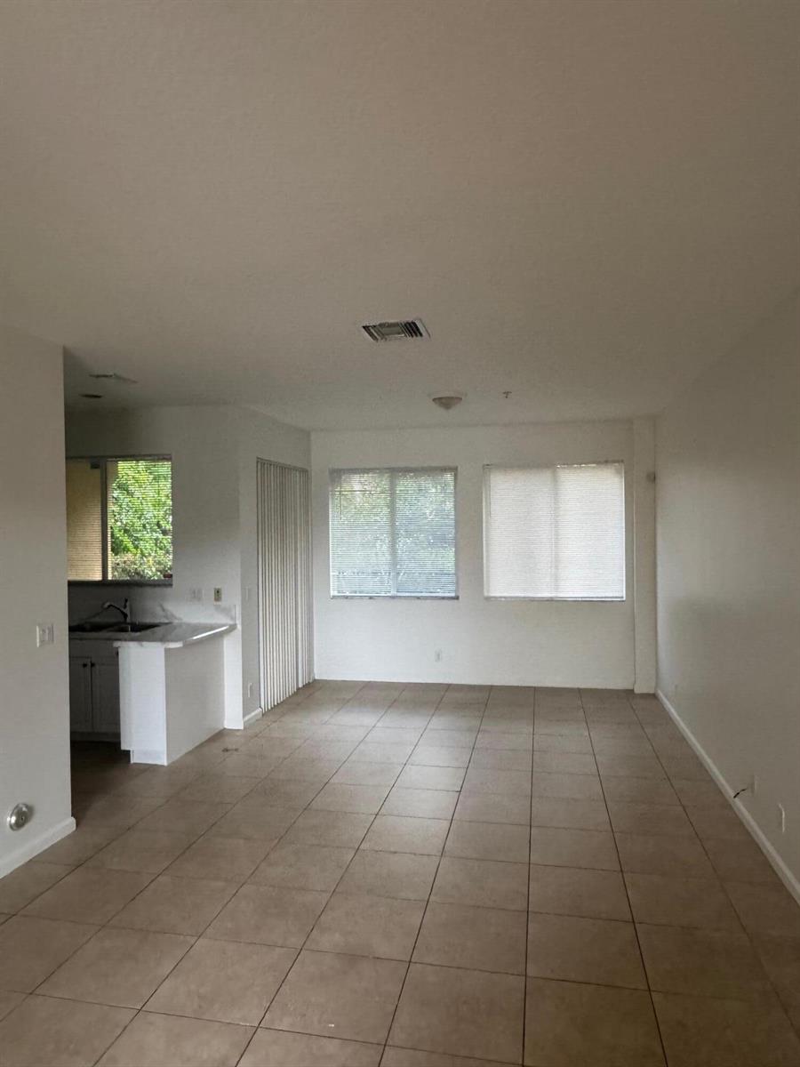 An open-concept living area features light-colored tile flooring, white walls, and a small kitchen — 4459 Cotswold Hills Drive, FL 33461, FL