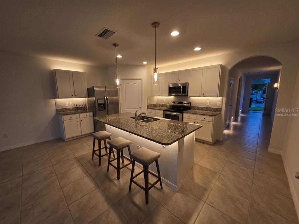 A kitchen with white cabinets, granite countertops, a central island with bar seating, and tile flooring — 2487 WHITE LILLY DRIVE, KISSIMMEE, FL