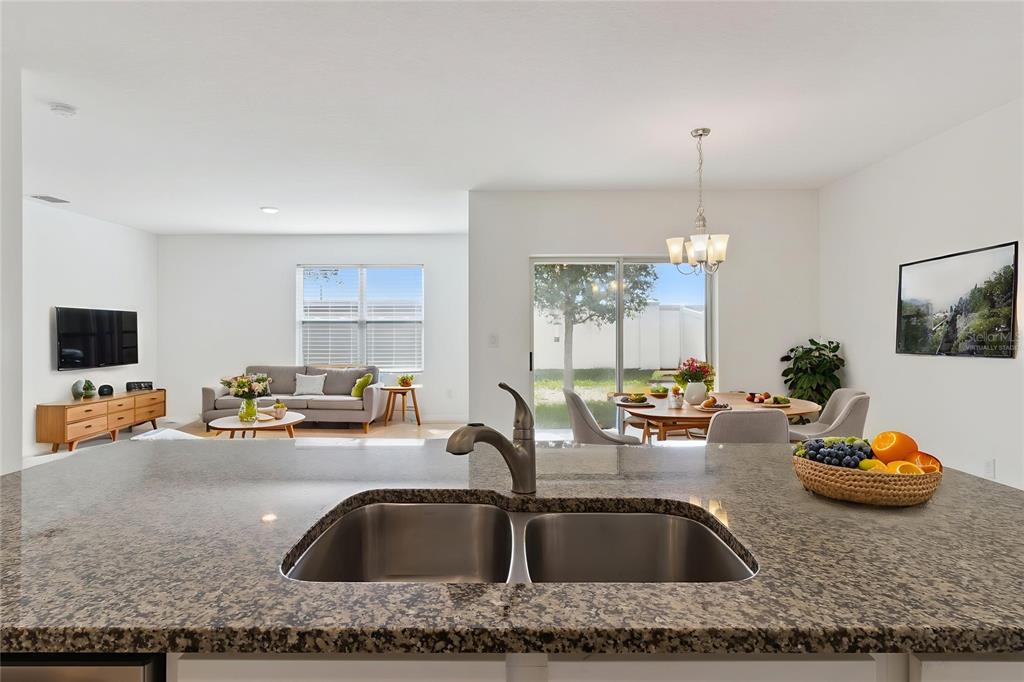 A kitchen island with a double sink overlooks an open-concept living and dining area — 2487 WHITE LILLY DRIVE, KISSIMMEE, FL