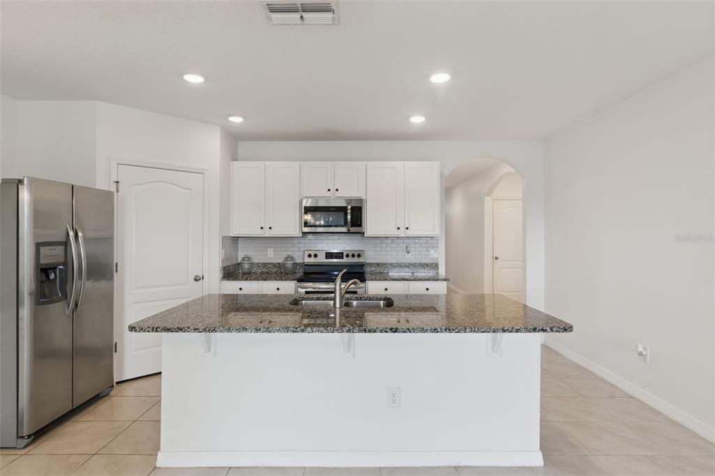 A kitchen features white cabinets, granite countertops, a central island, and stainless steel appliances — 2487 WHITE LILLY DRIVE, KISSIMMEE, FL