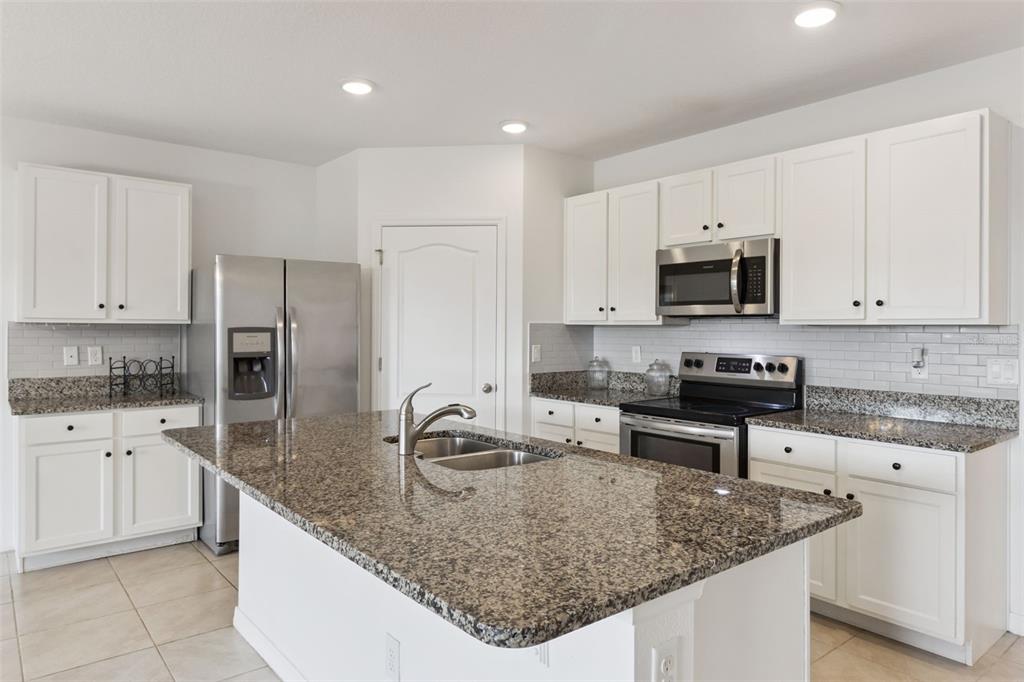 A kitchen features white cabinets, granite countertops, stainless steel appliances, and a central island — 2487 WHITE LILLY DRIVE, KISSIMMEE, FL