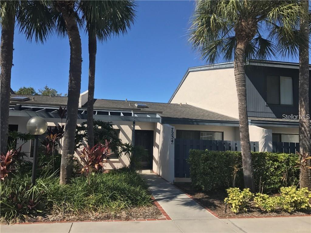 A single-story residential building with a walkway, palm trees, and a blue privacy fence — 7234 CLOISTER DRIVE UNIT 7234, SARASOTA, FL