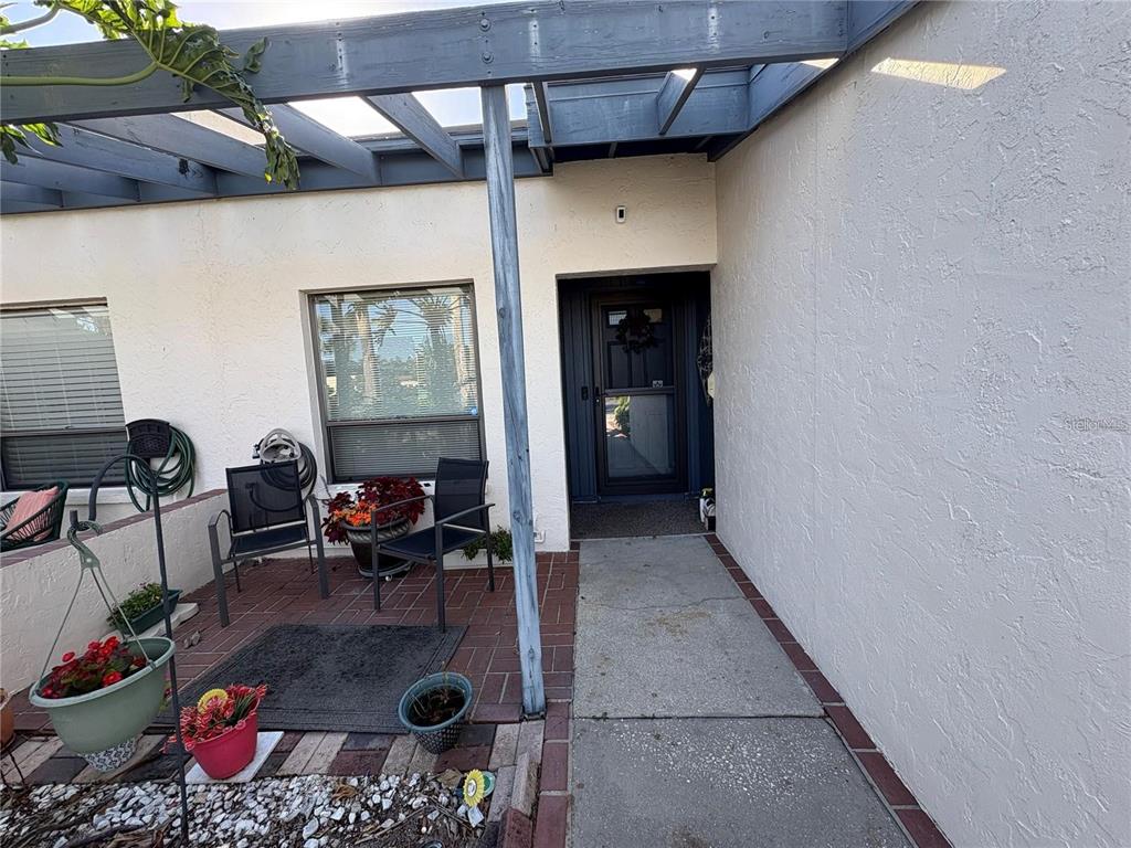 A concrete walkway leads to a front door under a blue wooden pergola — 7234 CLOISTER DRIVE UNIT 7234, SARASOTA, FL
