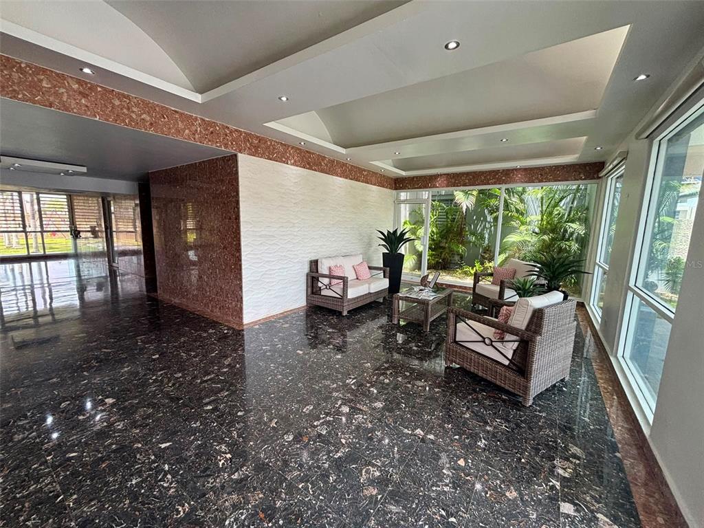 A sunroom with dark marble floors, a textured accent wall, and wicker furniture — 1005 Apt CONDOMINIO MUNDO FELIZ (10MO PISO - BALDORIOTY TOW UNIT 1005, CAROLINA, PR