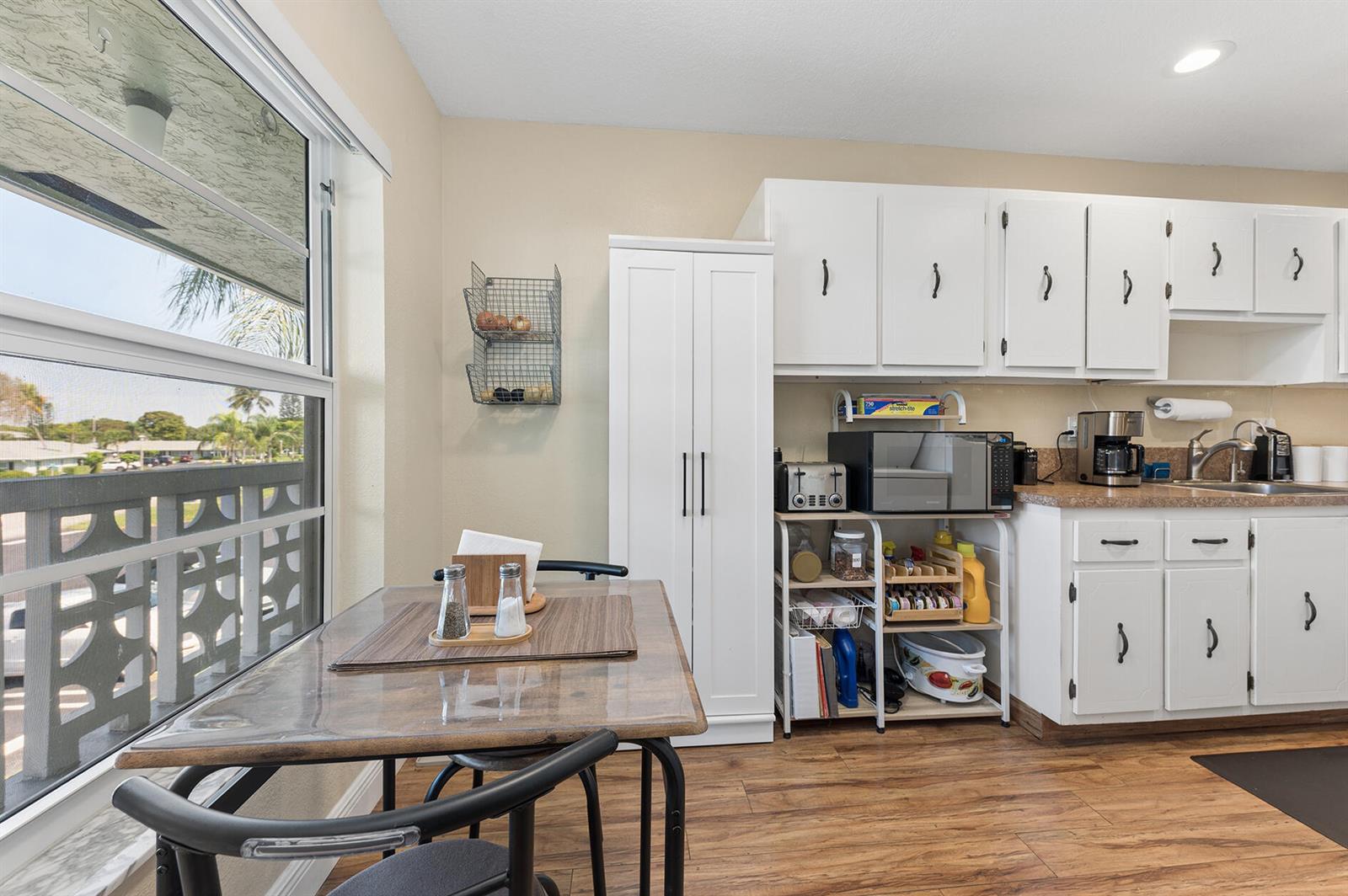 A kitchen features white cabinetry, a dining table by a window, and wood-look flooring — 1060 Citrus Way # 204, Delray Beach FL 33445, DELRAY BEACH, FL