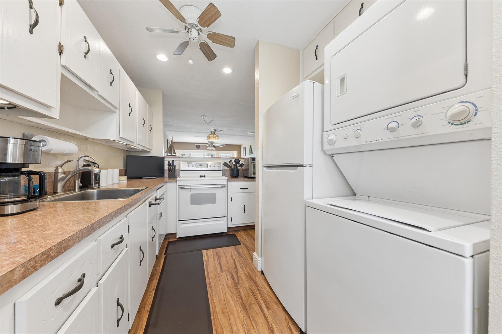 A galley kitchen features white cabinets, laminate countertops, a stacked washer-dryer, and wood-look flooring — 1060 Citrus Way # 204, Delray Beach FL 33445, DELRAY BEACH, FL