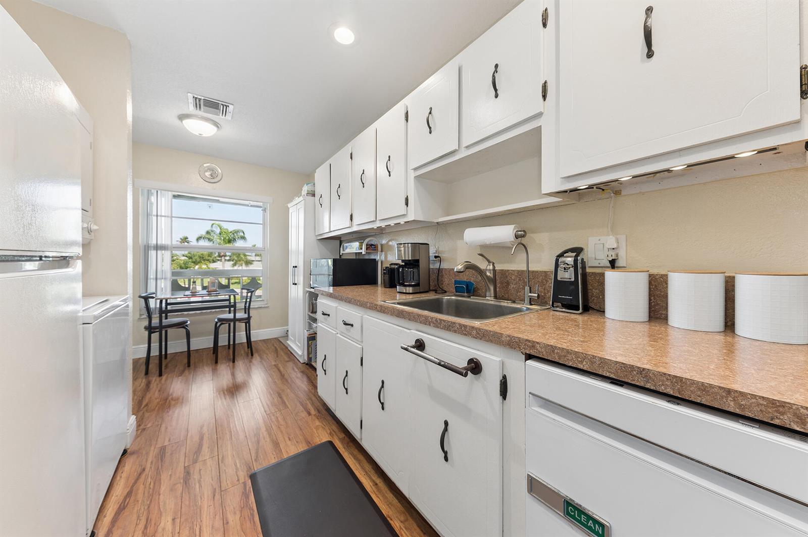 A kitchen features white cabinets, a brown laminate countertop, and a small dining area — 1060 Citrus Way # 204, Delray Beach FL 33445, DELRAY BEACH, FL