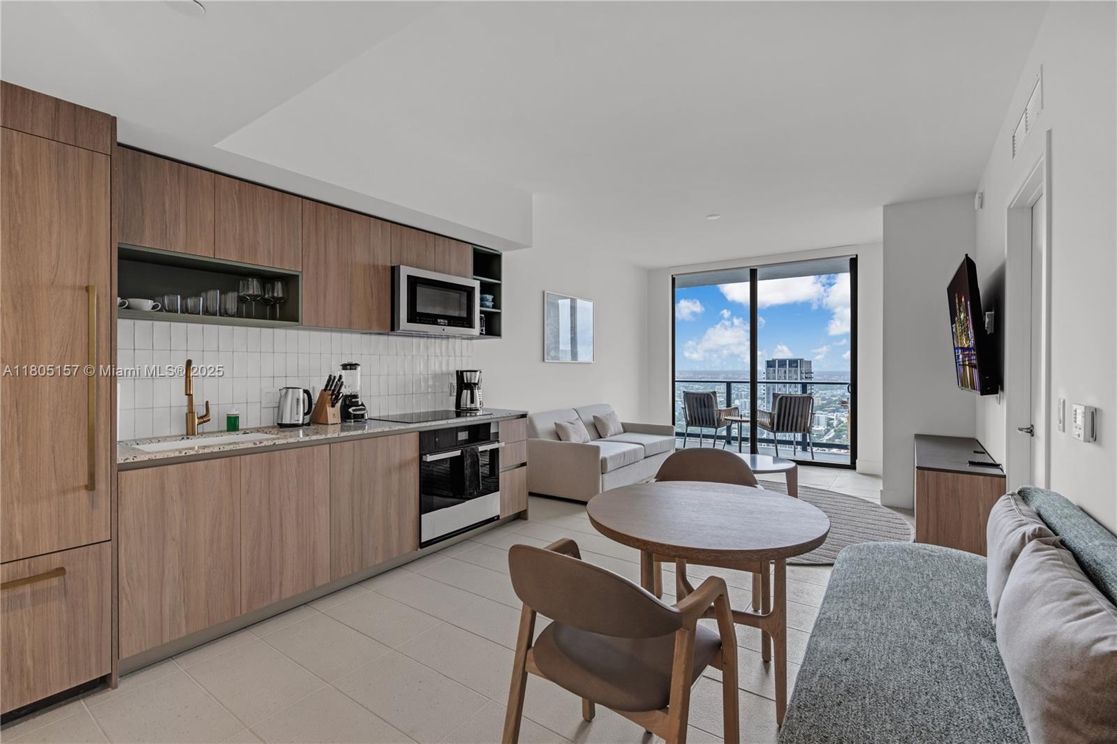 A modern kitchen and living area features wood cabinetry, a dining table, and balcony views — 601 NE 1st # 4204, Miami FL 33132, MIAMI, FL