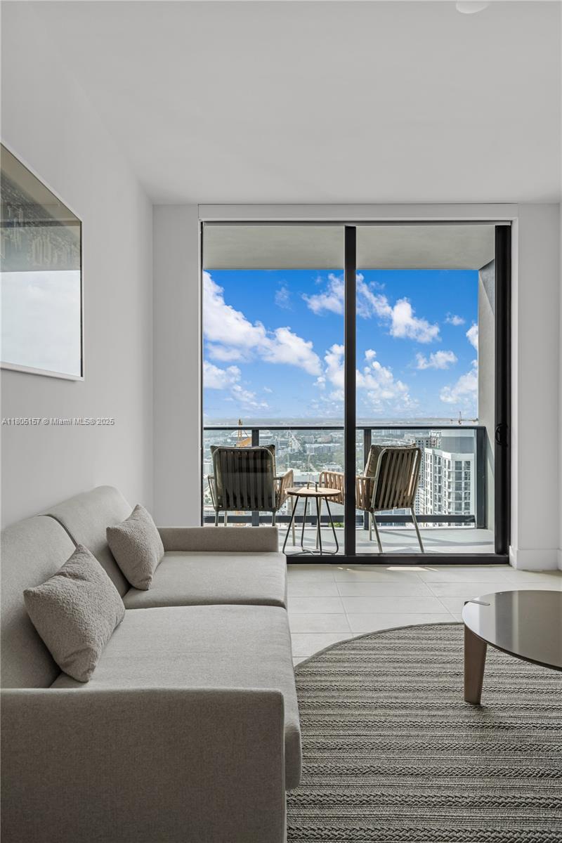 A living room features a light gray sofa, a round rug, and a balcony with city views — 601 NE 1st # 4204, Miami FL 33132, MIAMI, FL