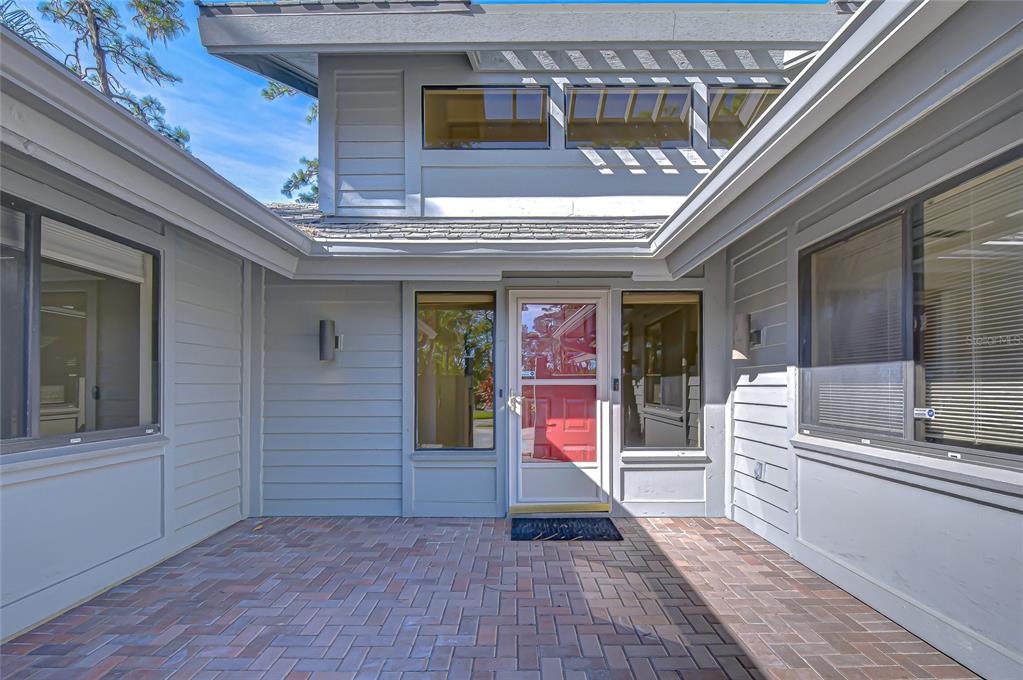 A brick-paved entryway leads to a gray house with a red front door — 5355 COBBLESTONE COURT, WESLEY CHAPEL, FL