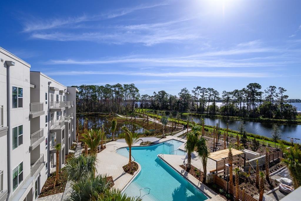 An elevated view of a swimming pool, apartment building, and a lake surrounded by trees — 11929 PIONEERS WAY UNIT A2, ORLANDO, FL