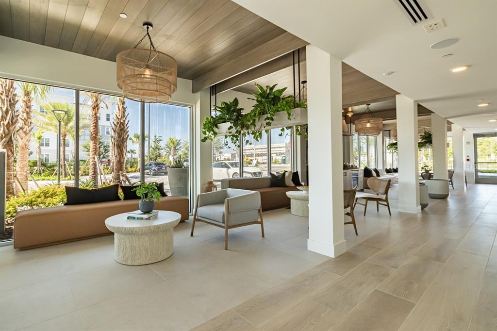 A modern lobby features floor-to-ceiling windows, wood-paneled ceilings, hanging plants, and contemporary lounge seating — 11929 PIONEERS WAY UNIT A2, ORLANDO, FL
